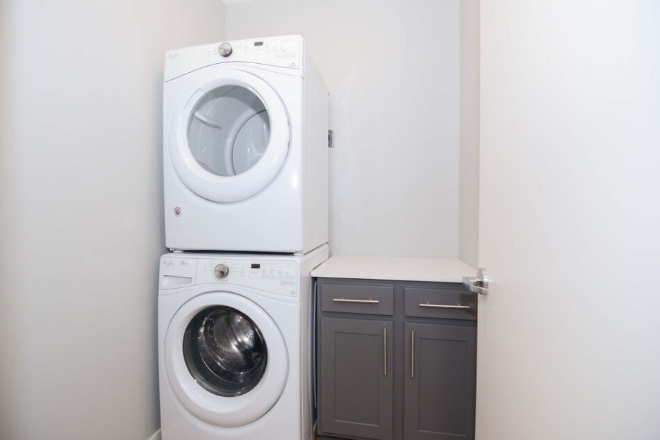 Stacked washer and dryer beside counter and cabinets.