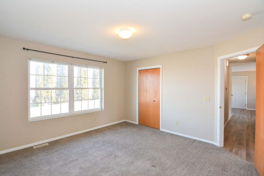 Bedroom with gray carpet and large windows.