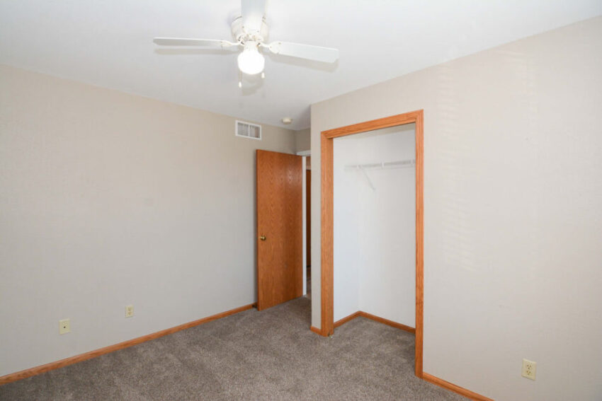 Bedroom with ceiling fan, beige walls, and wood-toned molding.
