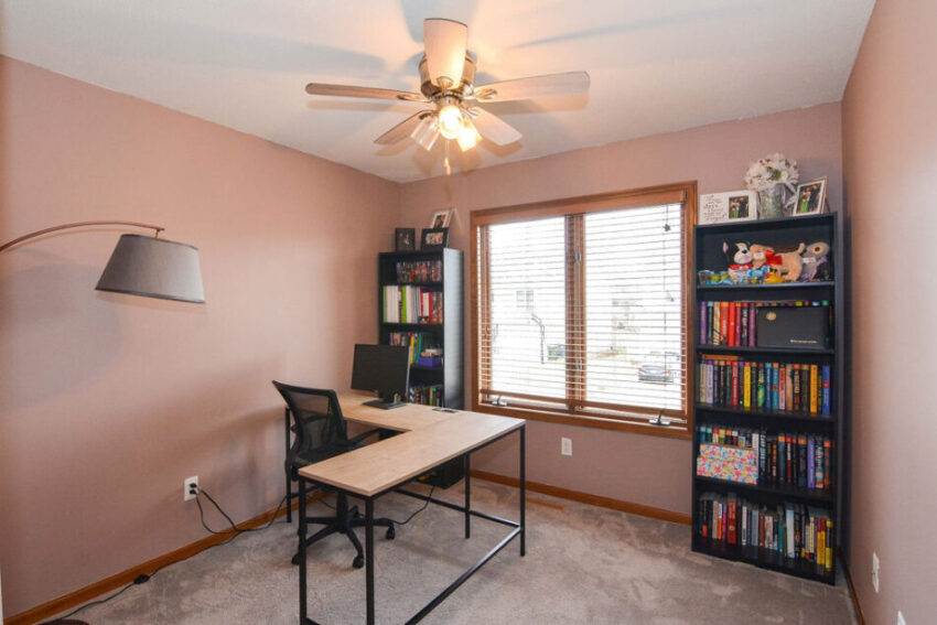 Office with large window, carpet, and ceiling fan.
