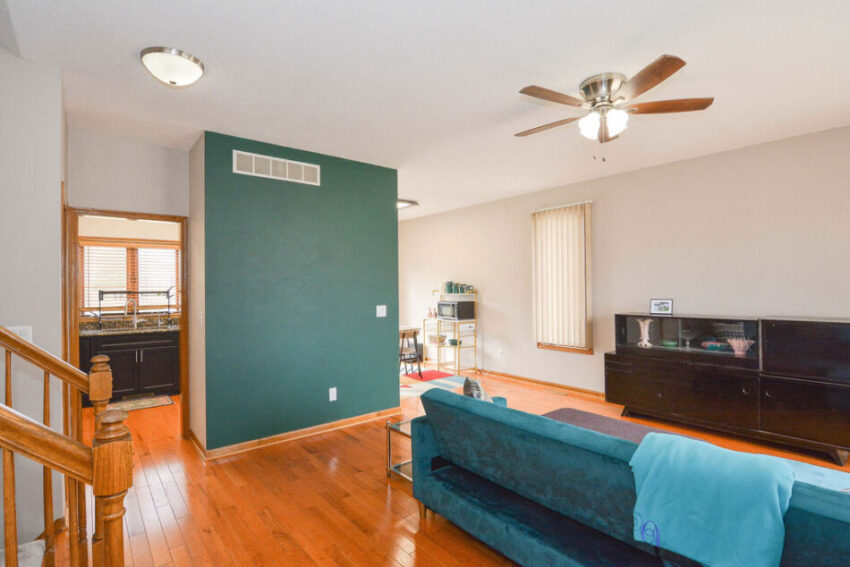 Living room with teal accent wall, oak floors, and ceiling fan.