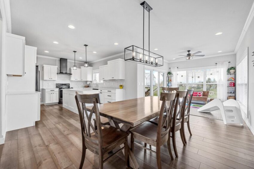 Dining area with chandelier with large kitchen in the background.