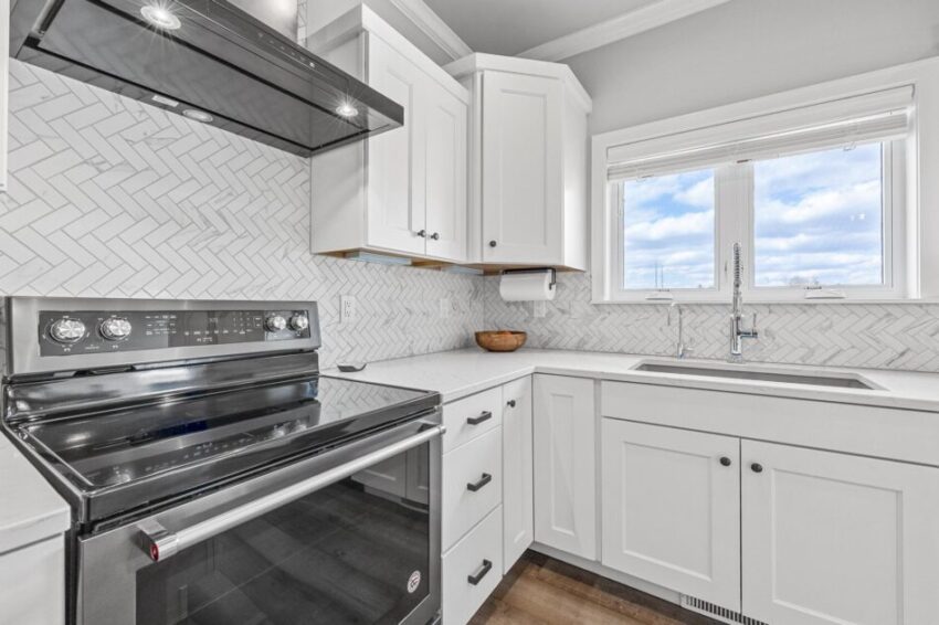 White corner cabinets and stainless steel oven in bright white kitchen.