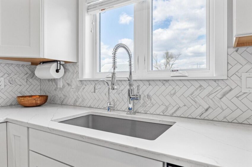 Gray and white herringbone backsplash behind sink in gorgeous kitchen.