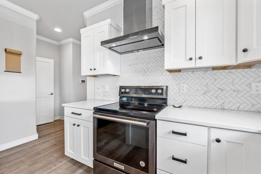 Stainless steel hood and range with white and gray backsplash.