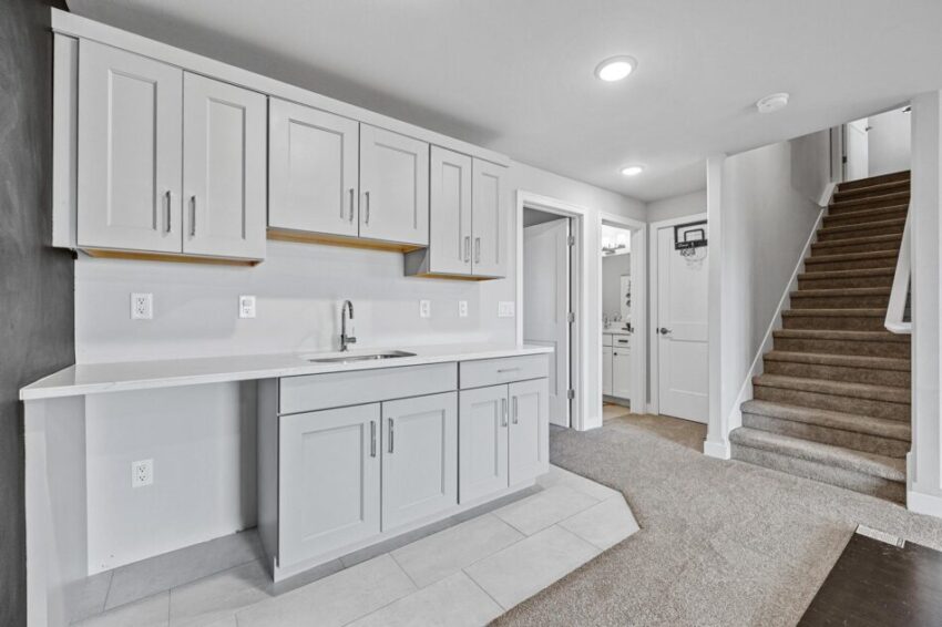 Wet bar in basement with gray cabinets and sink.