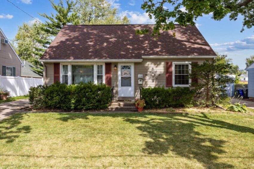 Cute home with landscaping, beige siding and grassy lawn.