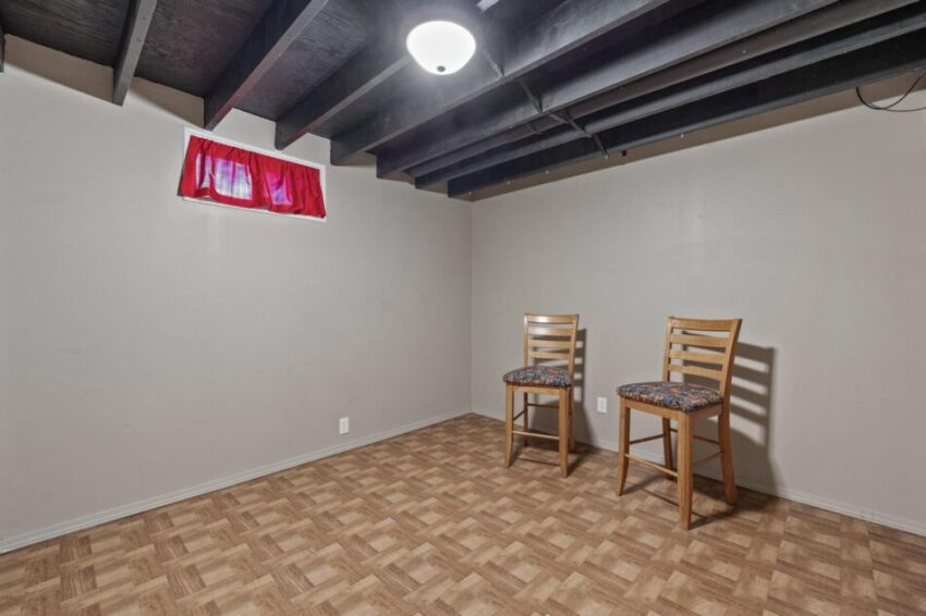 Finished lower level with painted ceiling beams and beige walls.