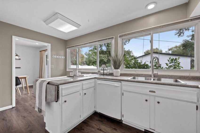 Kitchen with fold-out counter section, bright white cabinets, and stainless sink with large window.