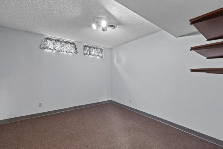 Lower level room with overhead light fixture, finished dark floor, and high windows.