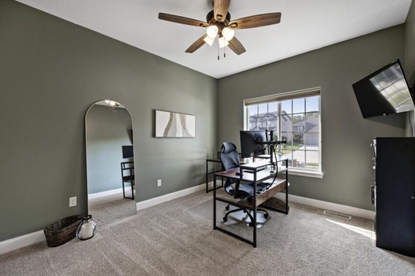 Office with gray/green walls, ceiling fan, and beige carpet.