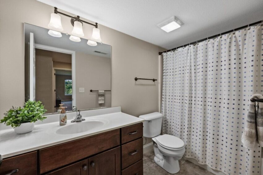 Third bathroom with shower curtain, dark cabinets, and large mirror.