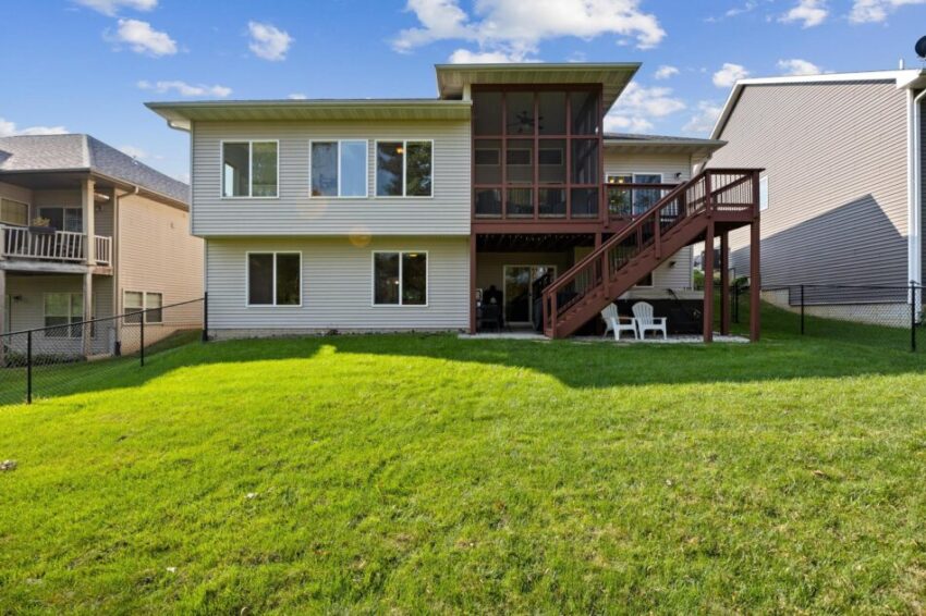 View of house from back with grassy lawn and sitting area beneath deck.