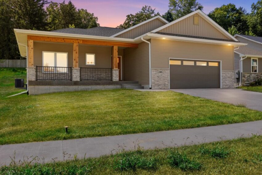 House with glowing windows, pristine lawn, and concrete drive.