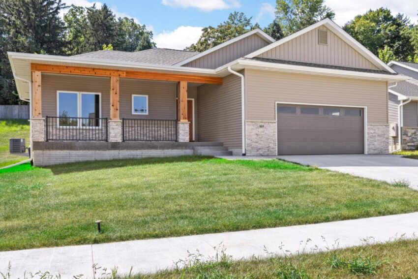 New construction home with tan siding, stone details, and wood porch beams.
