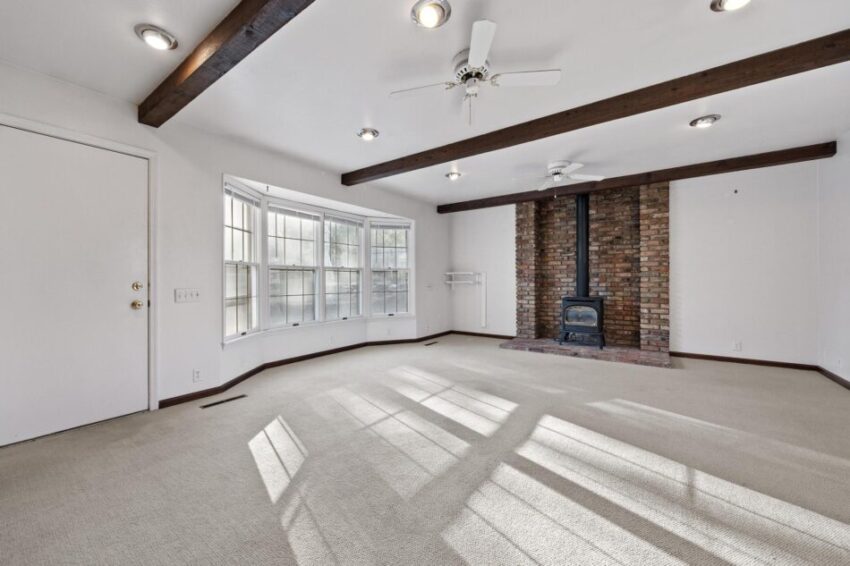 Living room with wood-burning fireplace, bay windows, and ceiling fan.