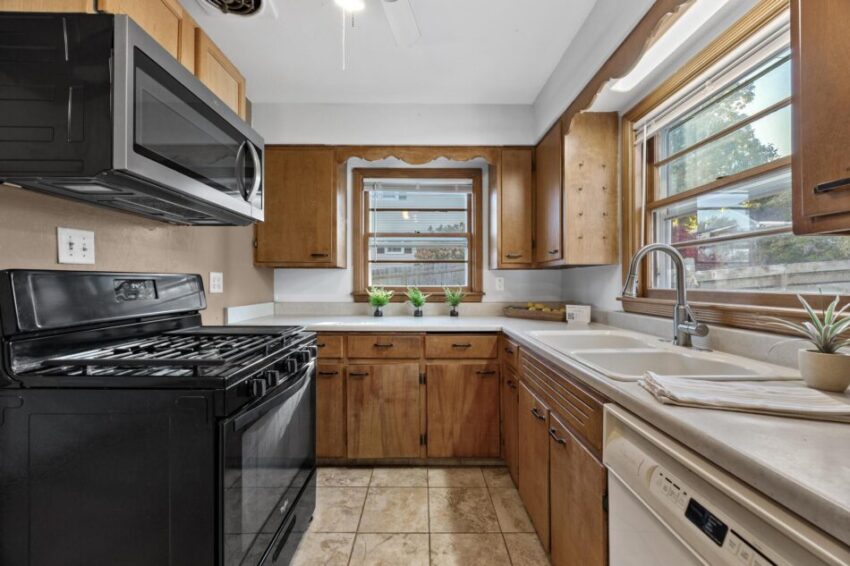 Kitchen with black stove and microwave, beige countertops, and windows above sink.