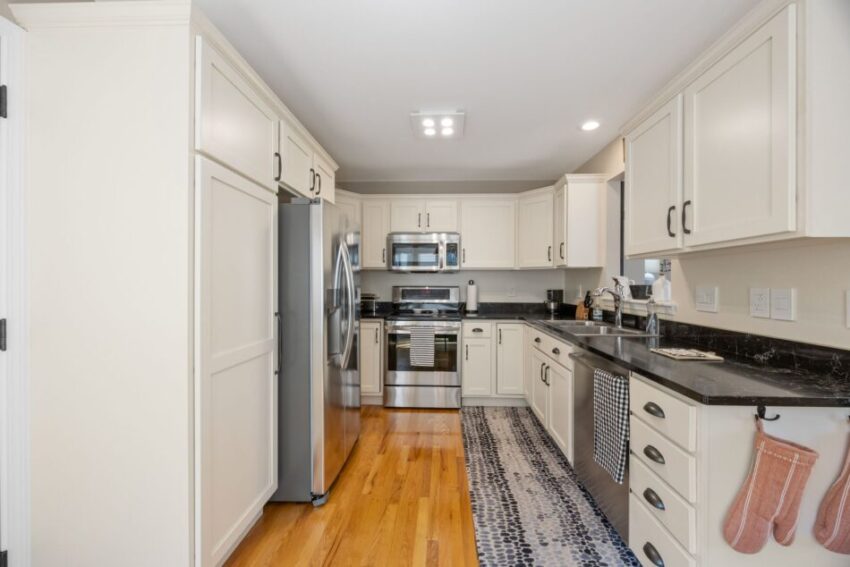 Modern kitchen with white cabinets, stainless steel appliances, and wooden floor.