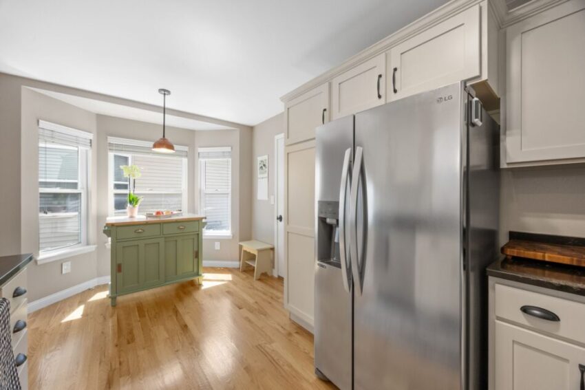 Bright kitchen with stainless steel fridge, green island, and wooden floor.