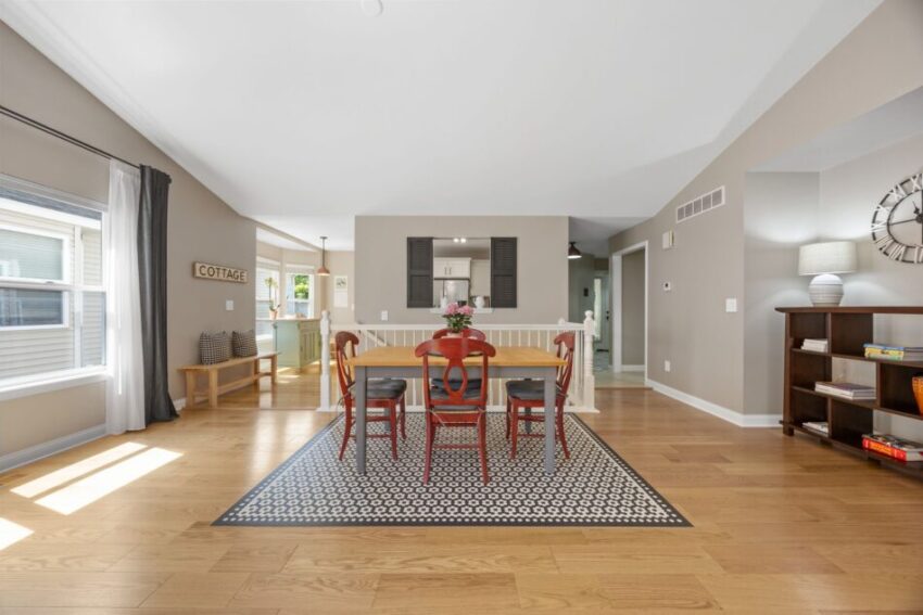 Dining area with wooden table, red chairs, and patterned rug in a bright room.