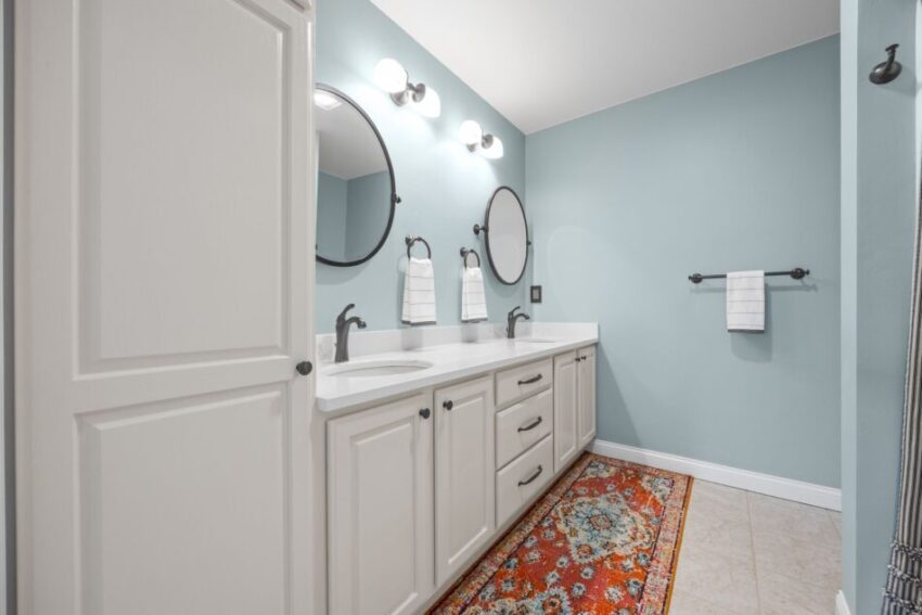 Bathroom with double sinks, round mirrors, and a colorful rug.