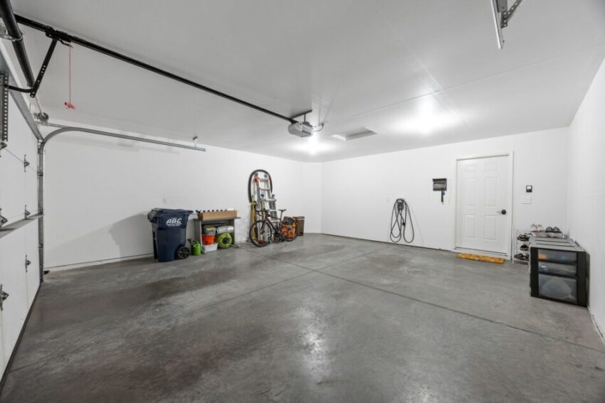 Empty garage with tools, recycling bins, and a ladder against the wall.