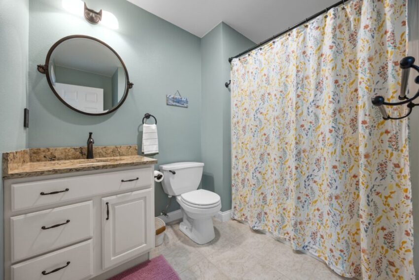 Bathroom with round mirror, floral shower curtain, and white vanity.