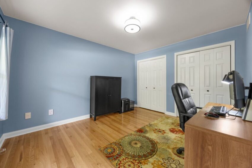 Home office with blue walls, wooden floor, desk, chair, and colorful rug.