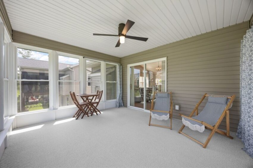 Sunlit enclosed porch with chairs, table, and ceiling fan.