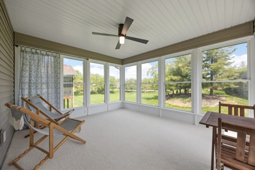 Sunlit three-season room with large windows, two chairs, and a ceiling fan.