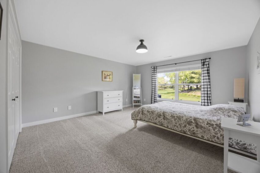 Spacious bedroom with bed, dresser, and large window overlooking greenery.