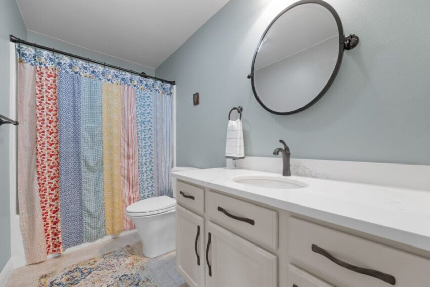Bathroom with colorful shower curtain, round mirror, and white vanity.