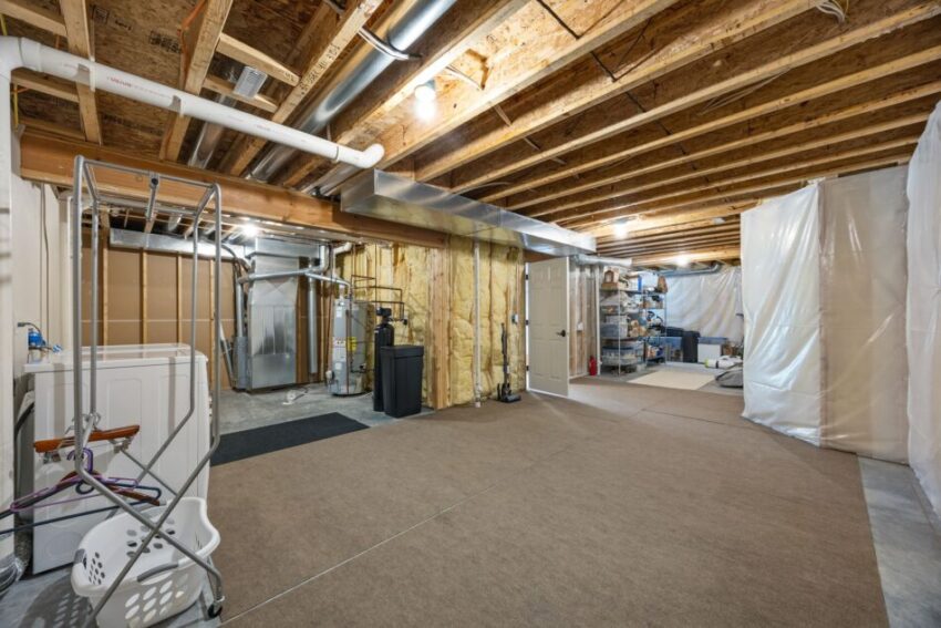 Unfinished basement with exposed beams, laundry area, and storage shelves.