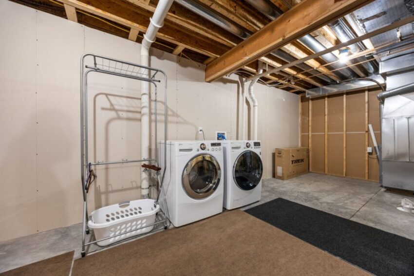 Basement laundry room with washer, dryer, and storage rack.