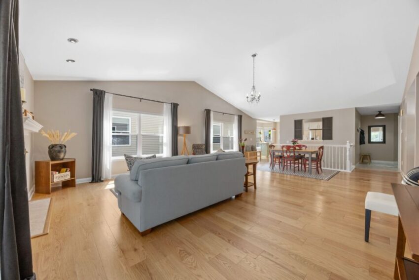 Spacious living room with wooden floor, gray sofa, and dining area.
