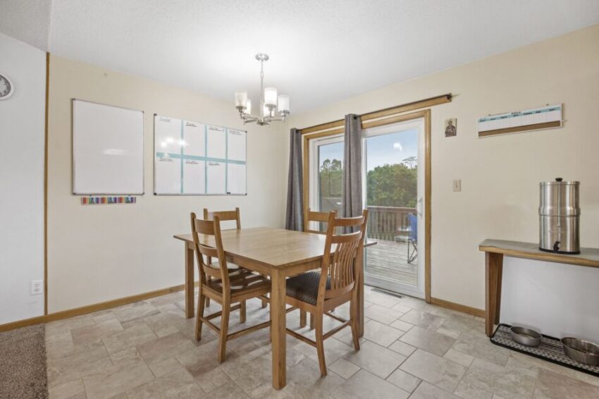 Dining area with wooden table, chairs, whiteboards, and sliding glass door to deck.