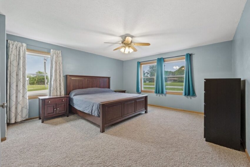 Bedroom with a bed, nightstand, dresser, and windows with blue curtains.