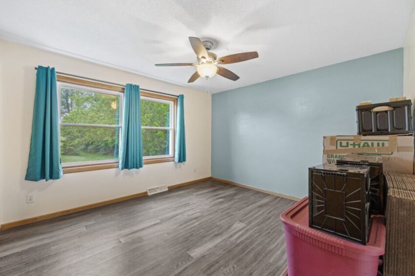 Empty room with blue accent wall, ceiling fan, and wood textured floor.