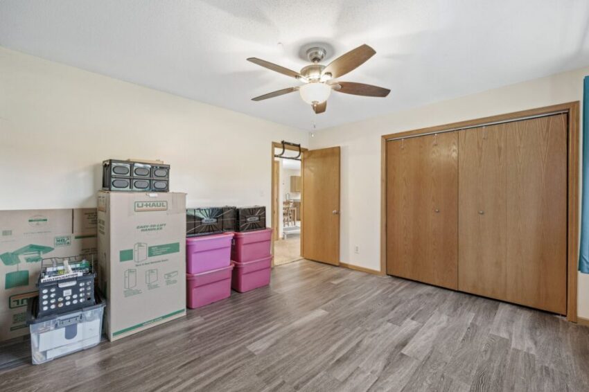 Empty room with ceiling fan, light walls, and closed wooden closet doors.
