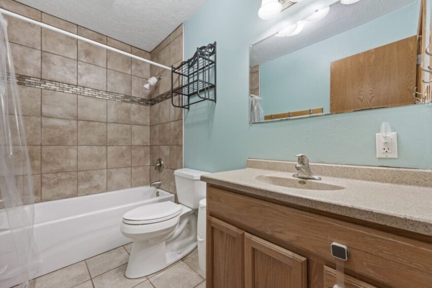 Bathroom with tiled walls, bathtub, toilet, and sink with mirror.