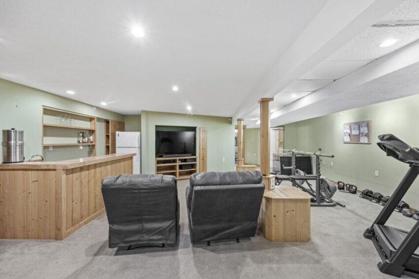 Basement with bar, seating, TV, exercise equipment, and light green walls.
