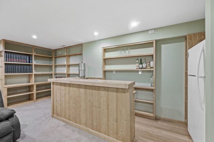 Home bar with wooden shelves, books, and a refrigerator.