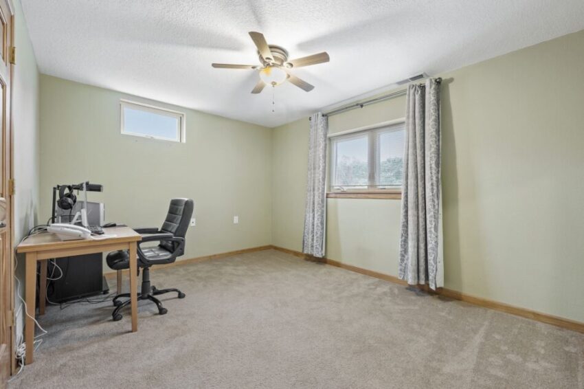 Home office with desk, chair, and ceiling fan in a carpeted room.