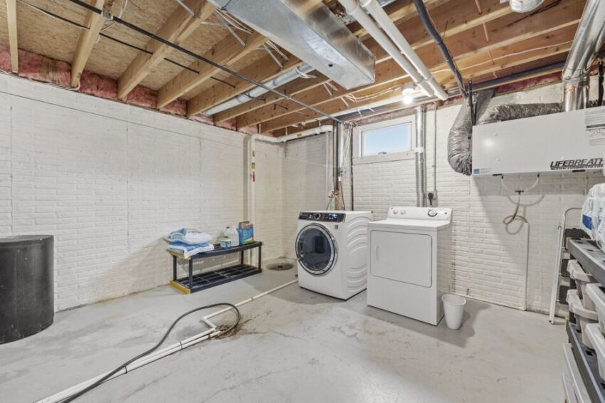 Basement laundry room with washer, dryer, and exposed ceiling beams.