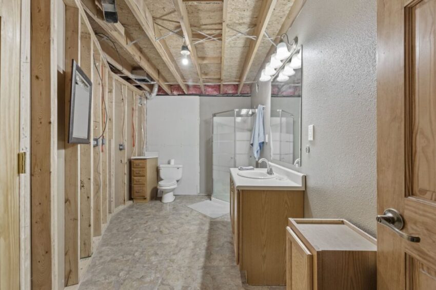 Unfinished bathroom with exposed ceiling, shower, toilet, and double sink vanity.