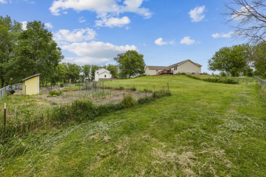 Spacious backyard with garden, trees, and a house under a blue sky.