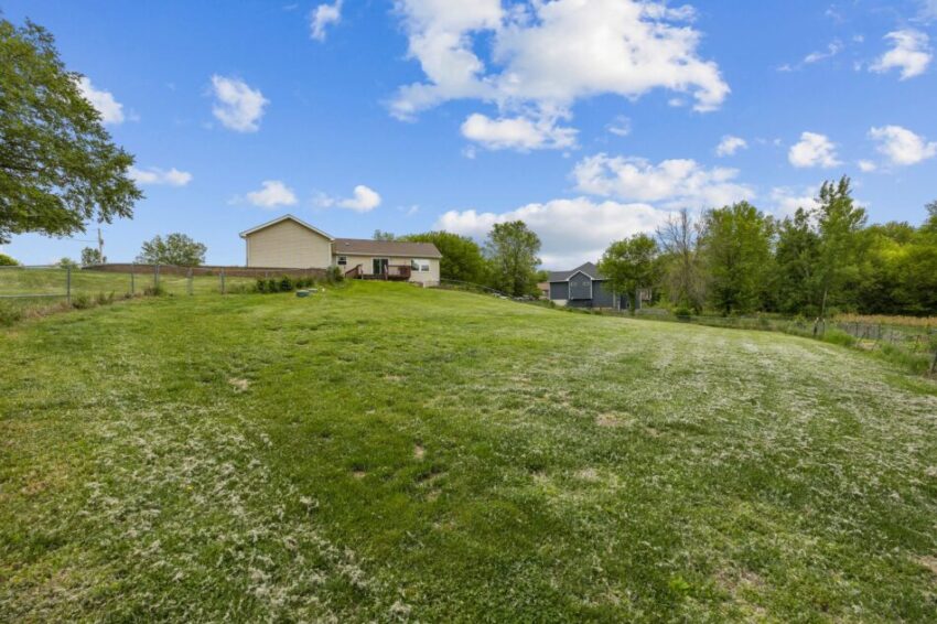 Spacious grassy backyard with a house and trees under a blue sky.