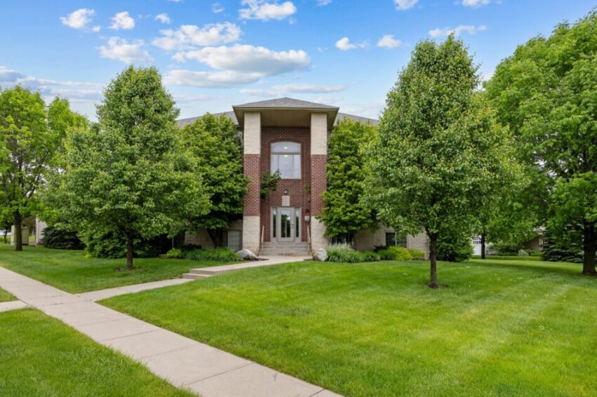A brick building surrounded by green trees and grass under a blue sky.