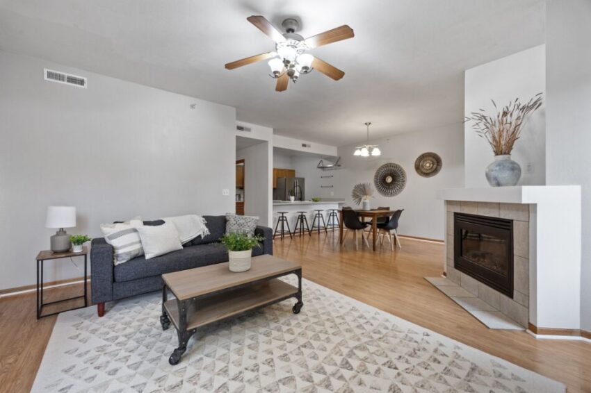 Modern living room with gray sofa, wooden table, and fireplace. Dining area in background.