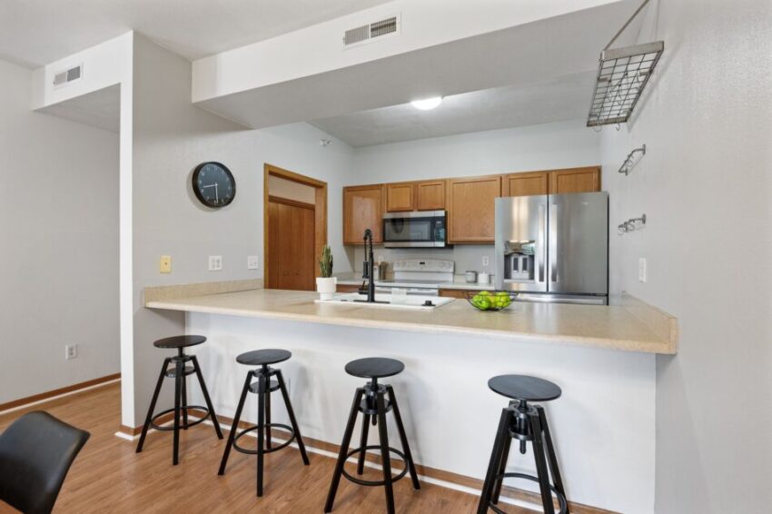 Modern kitchen with bar stools, wooden cabinets, and stainless steel appliances.